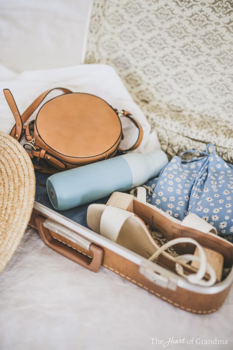 A partially packed suitcase on a bed with a straw hat.