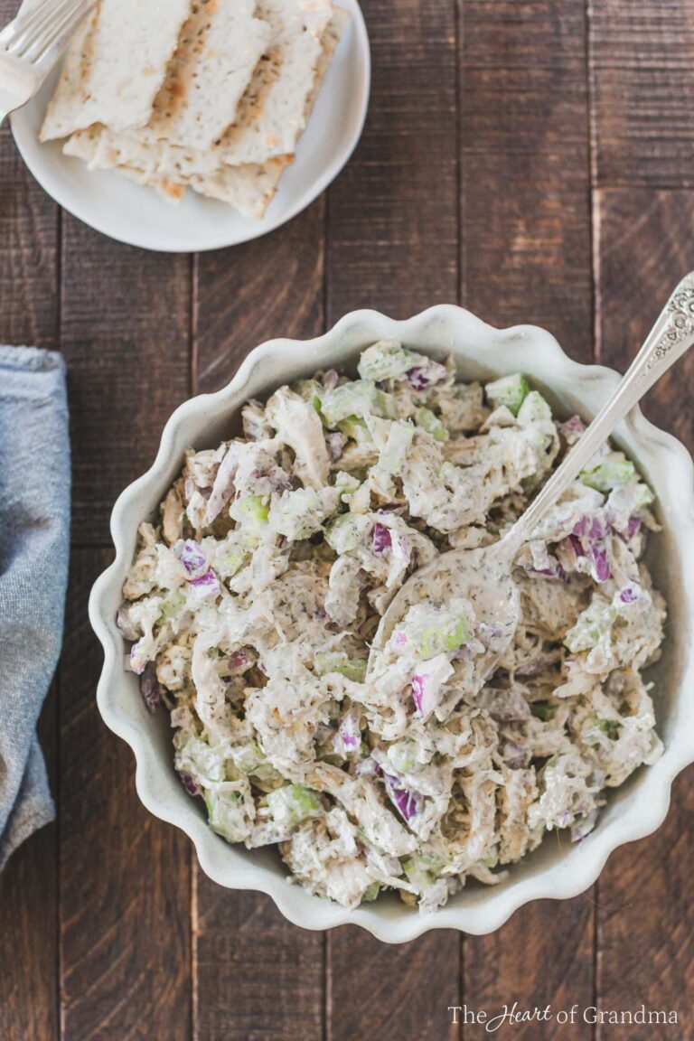 A bowl of chicken salad with a spoon in it and some crackers in the background.