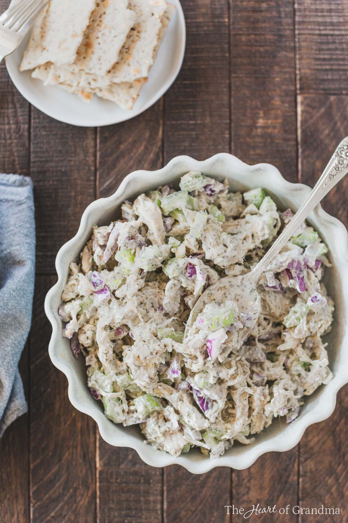 A bowl of chicken salad with a spoon in it and some crackers in the background.
