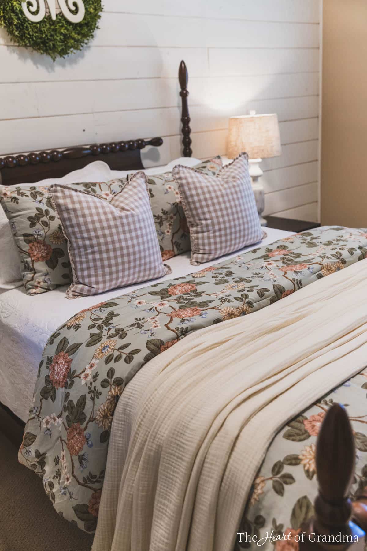 A spindle bed with green floral bedding and a green wreath on the wall behind it.