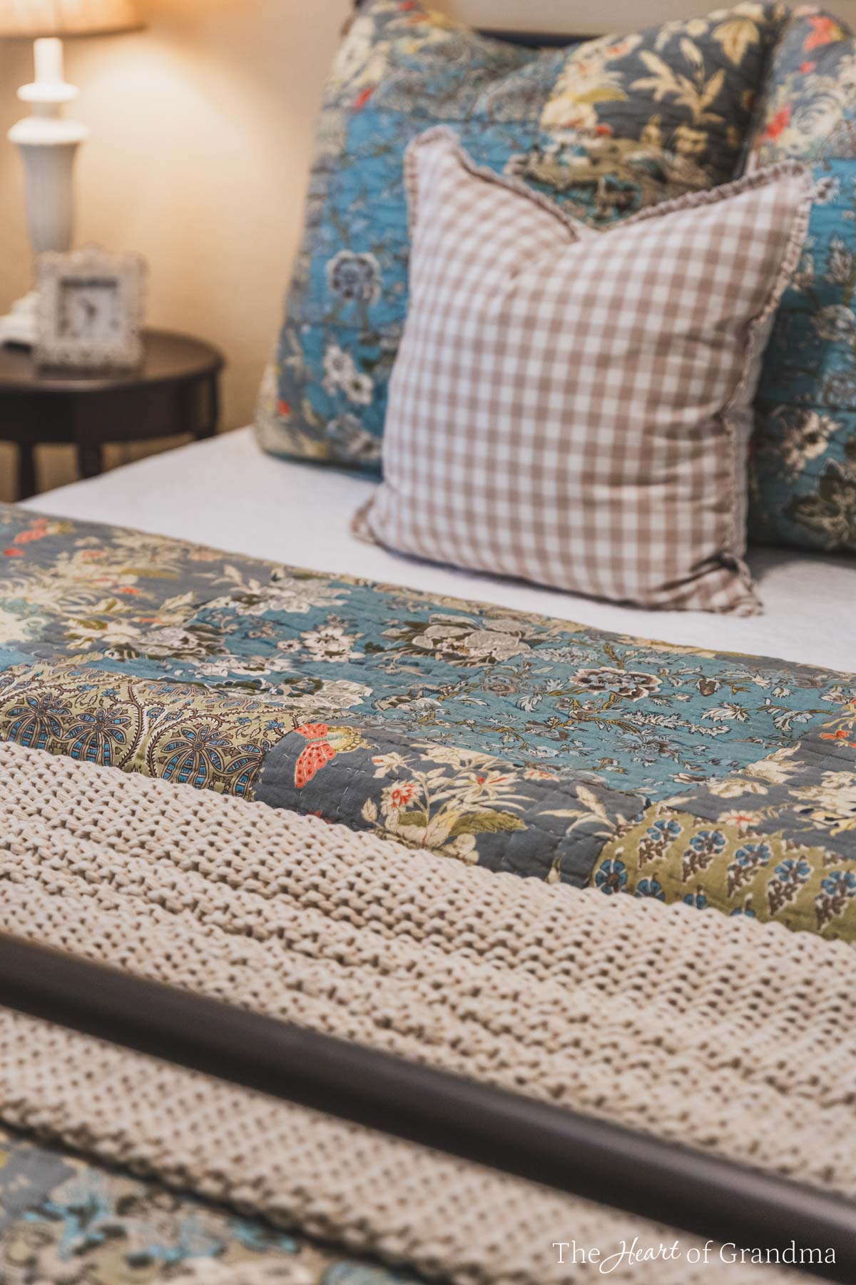 A bed with a blue floral quilt and a tan chunky blanket. 