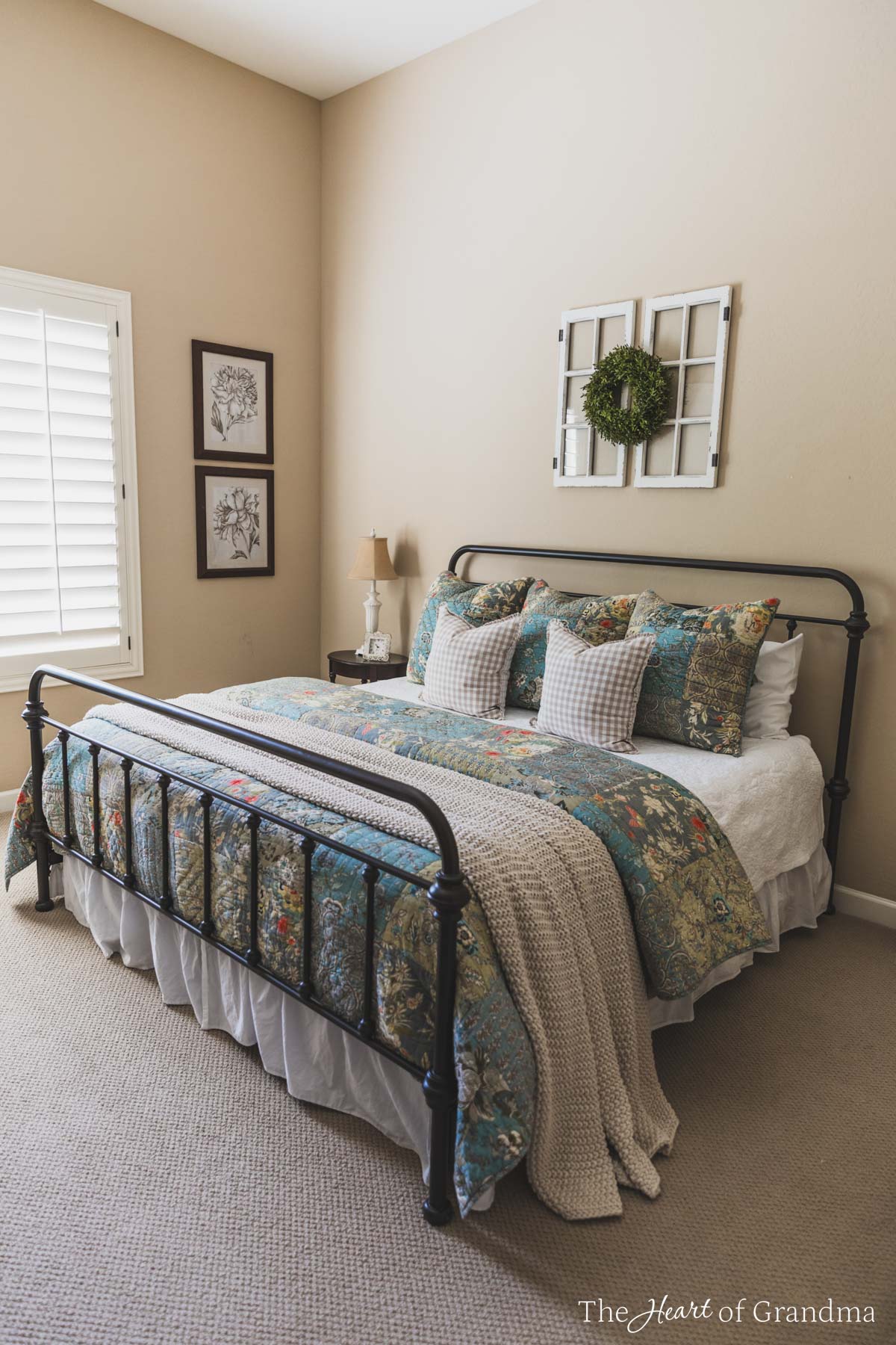 A metal bed made up with a grayish quilt and a tan knit blanket.