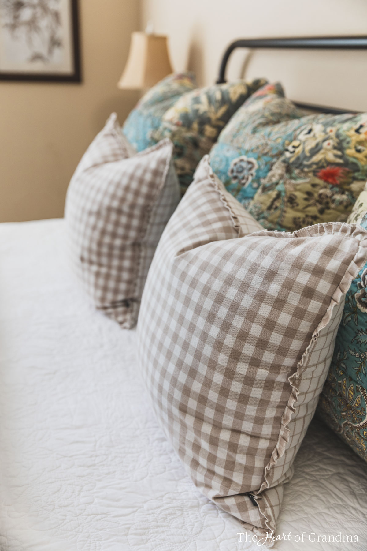 Pillows on a bed with a white quilt and a lamp in the background.