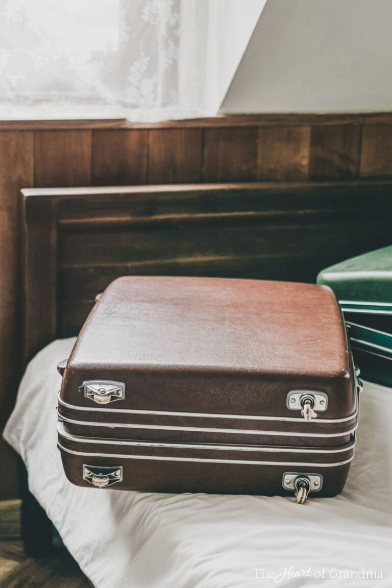 Two suitcases sitting on a bed in front of a window with a lace curtain.