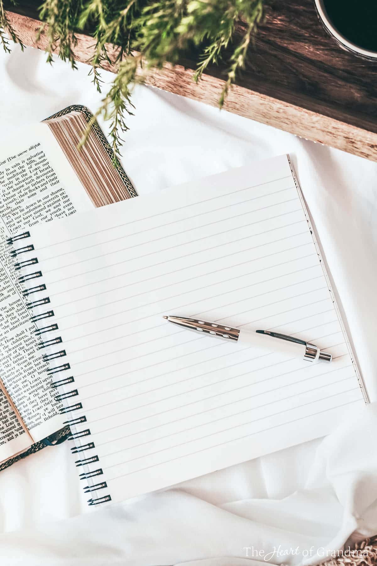 An empty note pad with a pen lying on a bed with a tray of coffee.