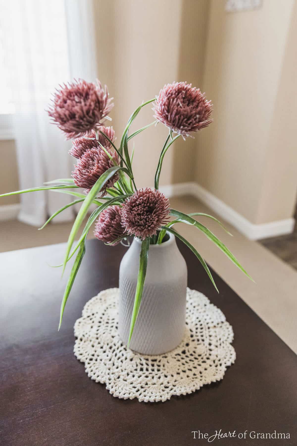 Flowers in a white vase sitting on a crochet doily.