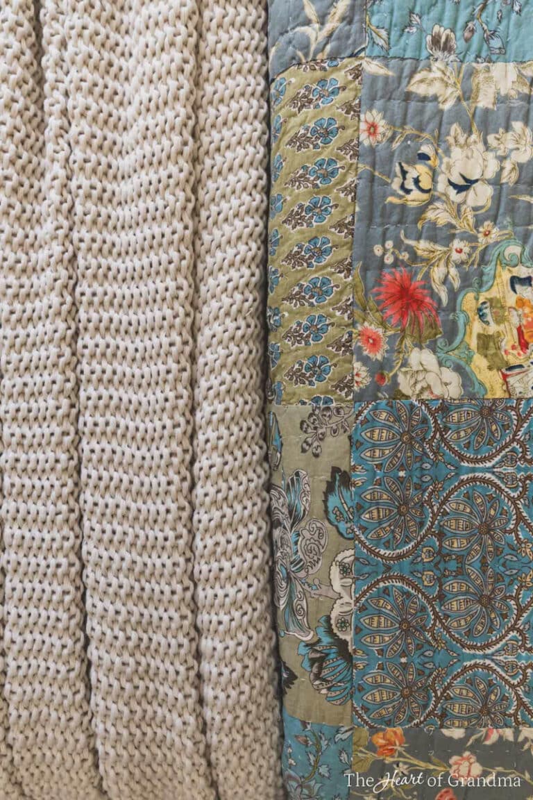 A bluish gray floral quilt laying with a chunky tan knit blanket.