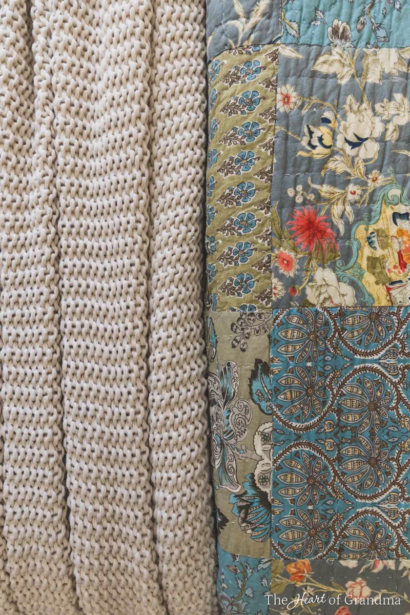 A bluish gray floral quilt laying with a chunky tan knit blanket.