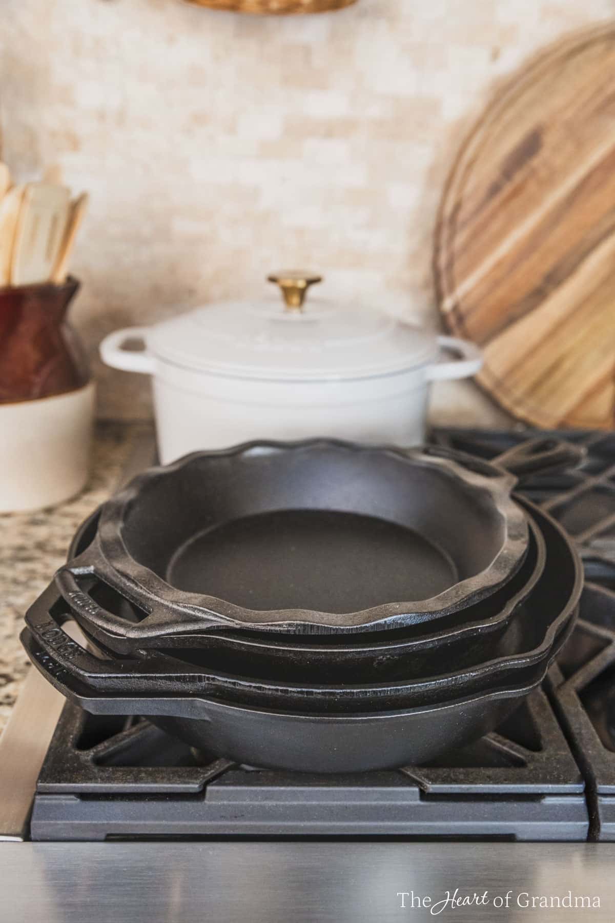 A stack of Lodge cast iron pans sitting on a gas cooktop with a Dutch oven and some wooden utensils in the background.