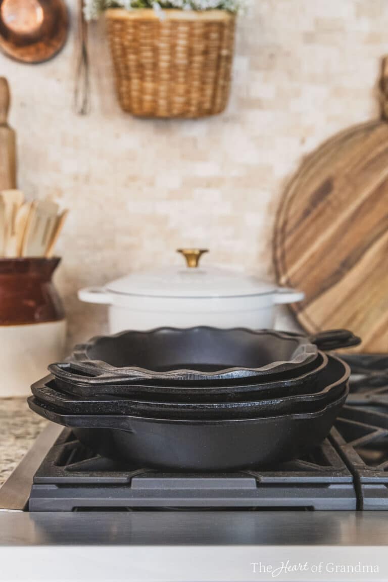 A stack of Lodge cast iron pans sitting on a gas cooktop with a Dutch oven and some wooden utensils in the background.