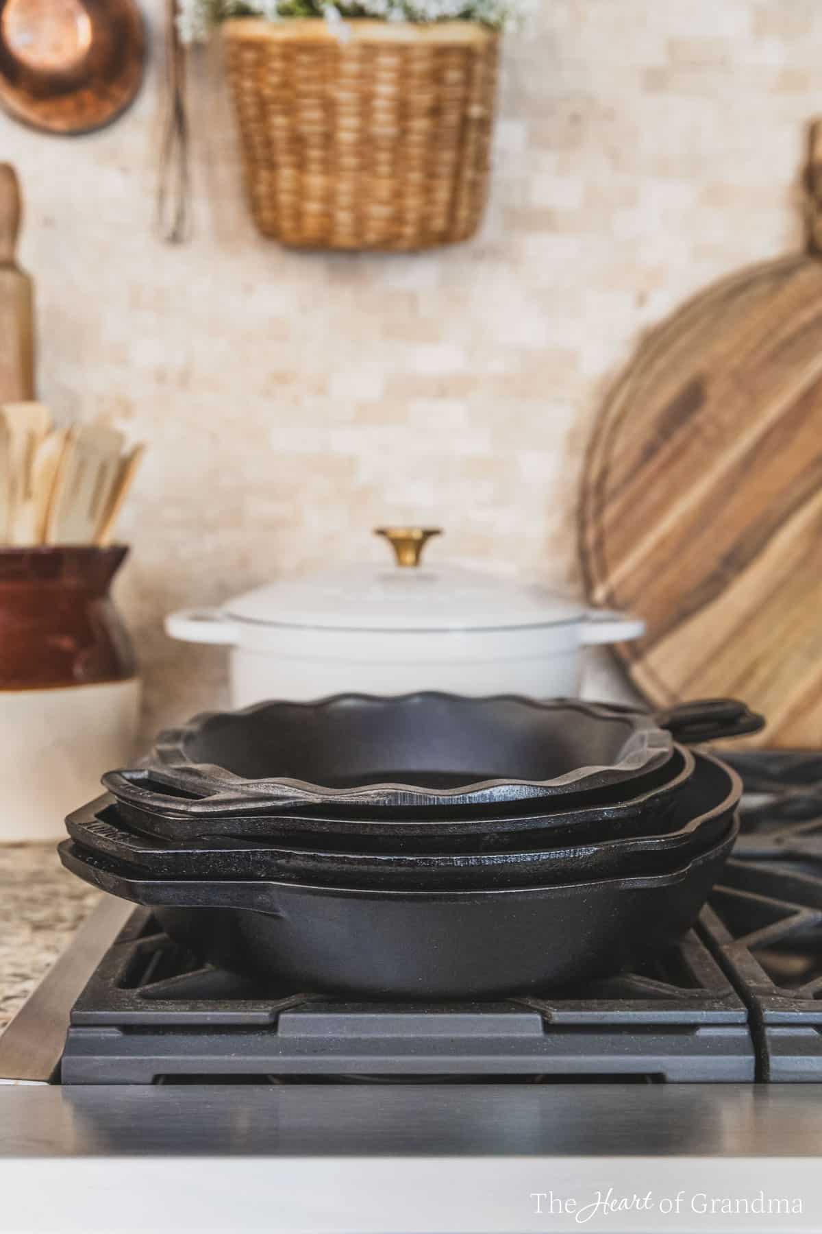 A stack of Lodge cast iron pans sitting on a gas cooktop with a Dutch oven and some wooden utensils in the background.
