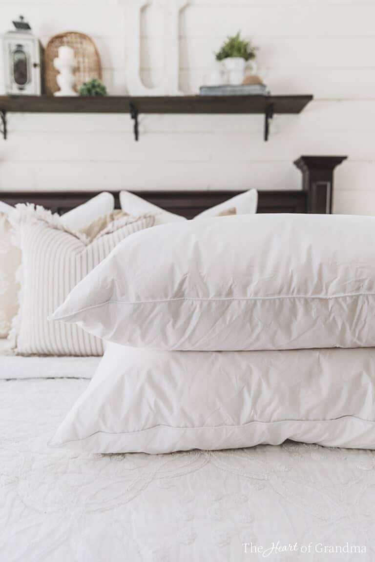 Two clean white pillows stacked on a made bed with a shelf in the background.