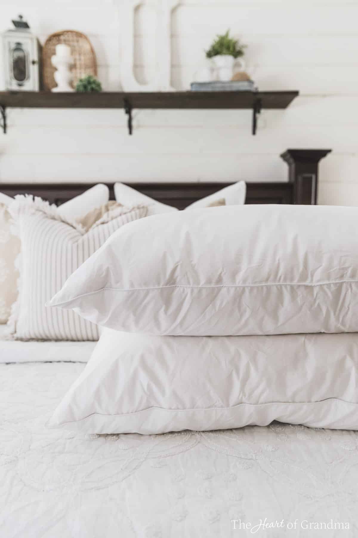 Two clean white pillows stacked on a made bed with a shelf in the background.
