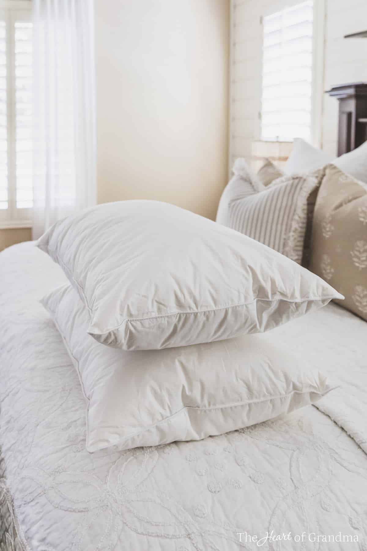 Two clean white pillows stacked on a made bed with a shelf in the background.