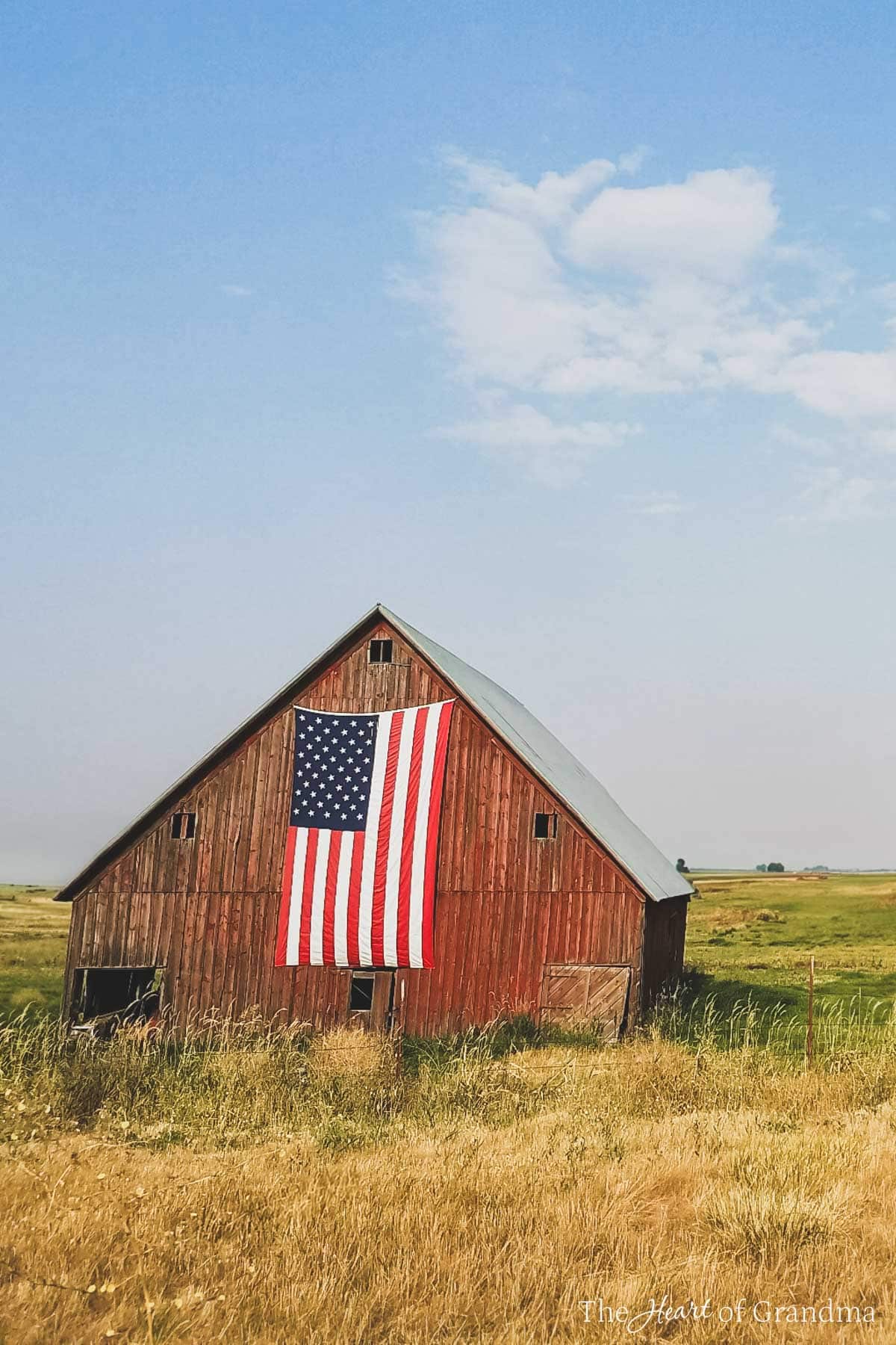 A red barn in a grassy field with an American flag hanging from the front.