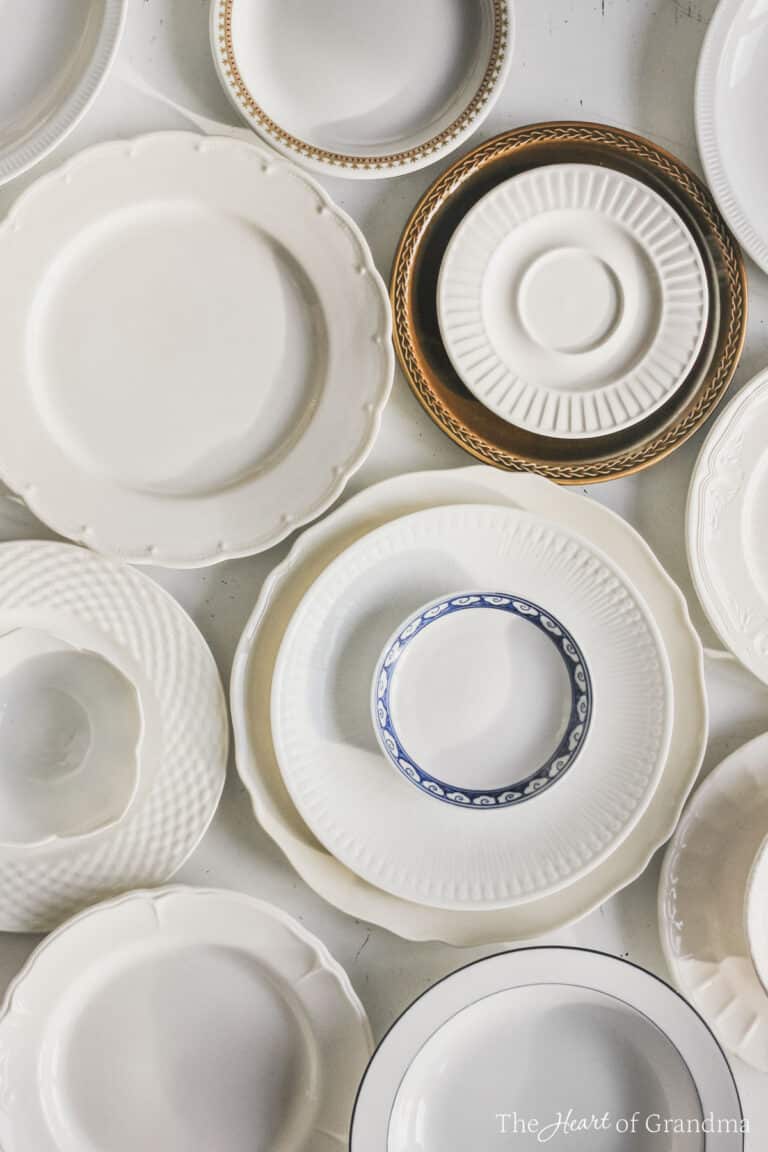 Antique plates laid out and stacked up on a white table.