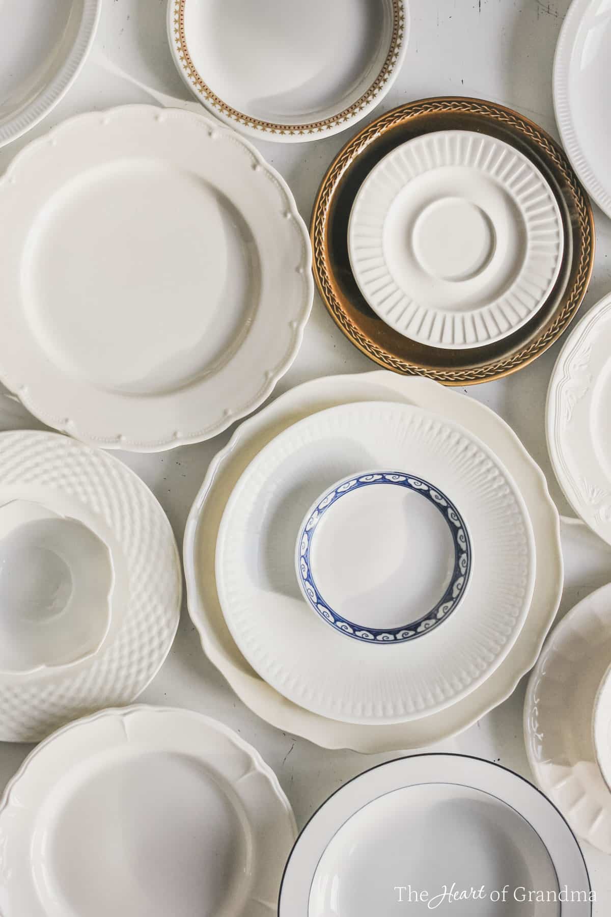 Antique plates laid out and stacked up on a white table.