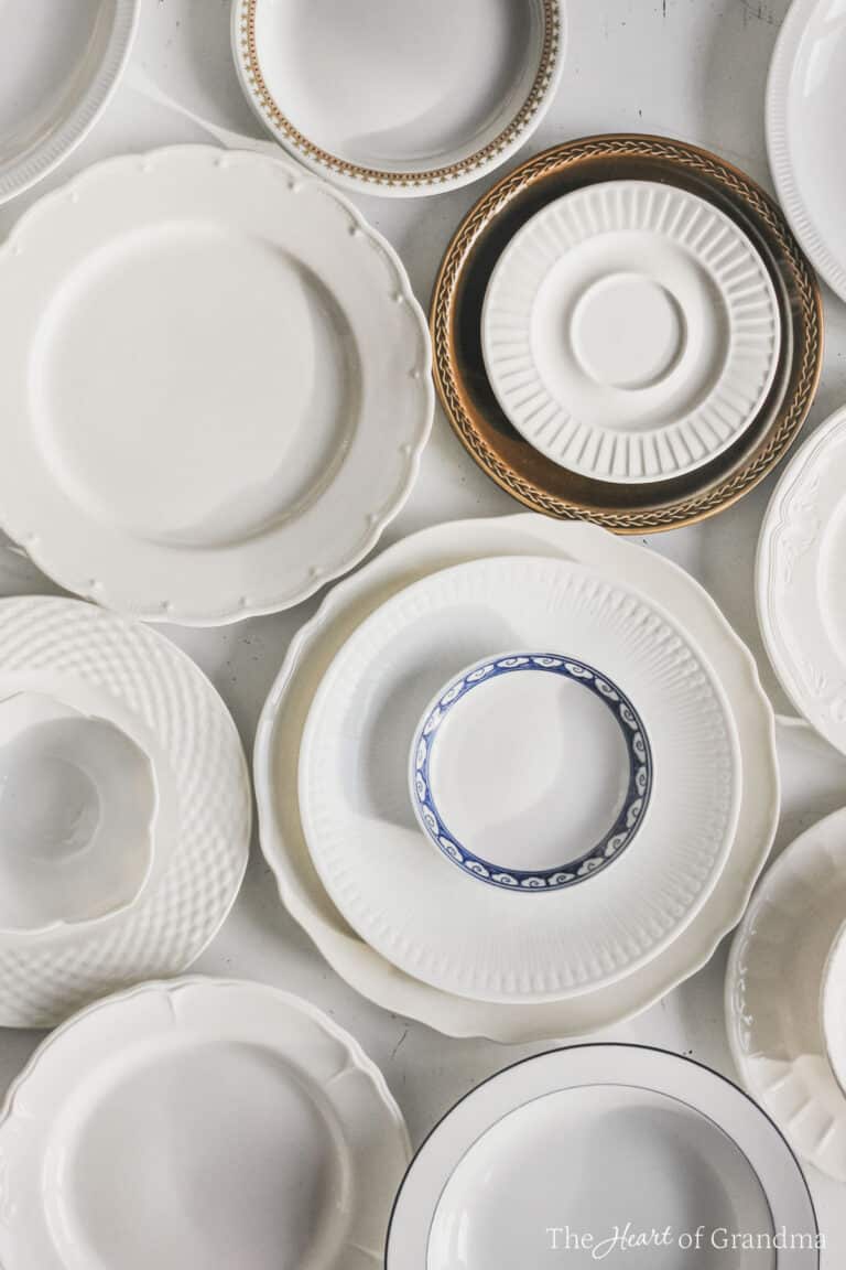 Antique plates laid out and stacked up on a white table.