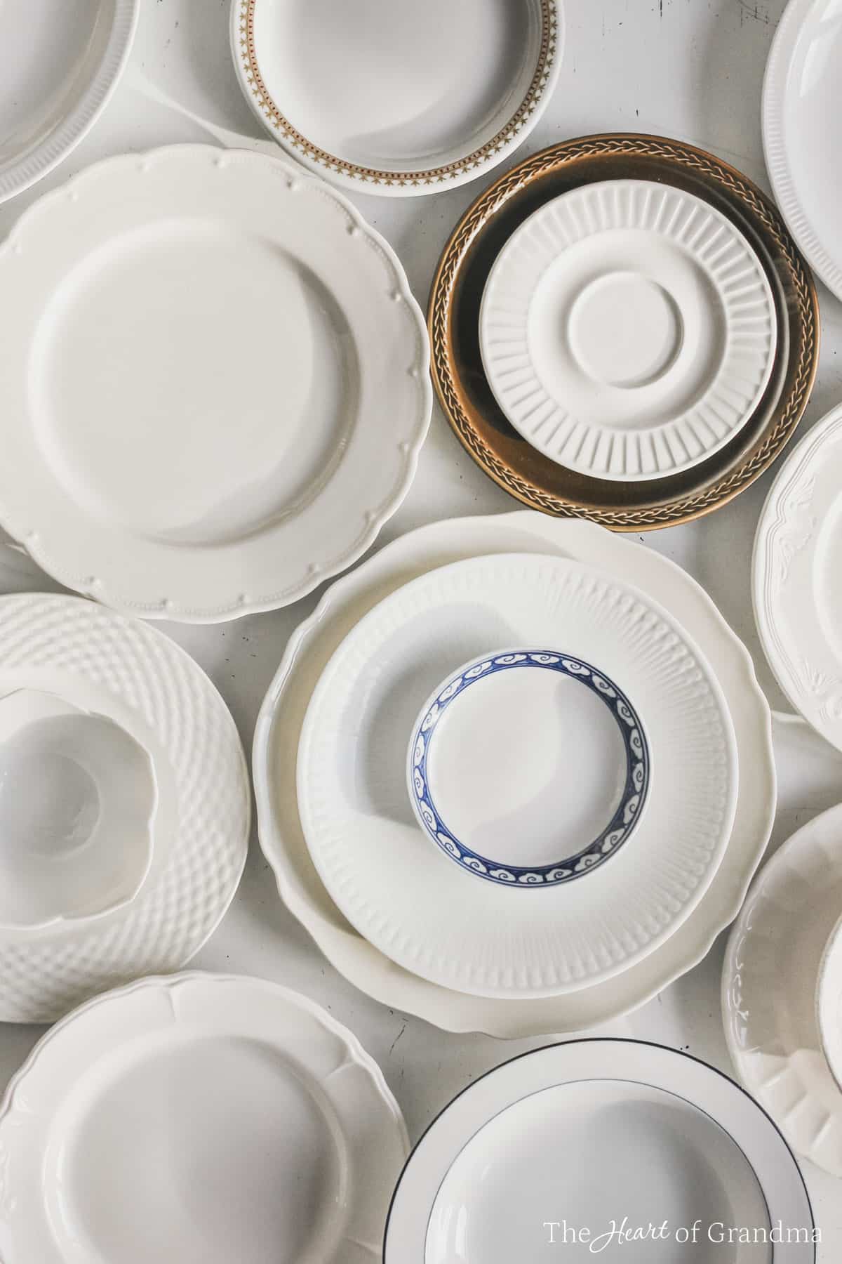 Antique plates laid out and stacked up on a white table.