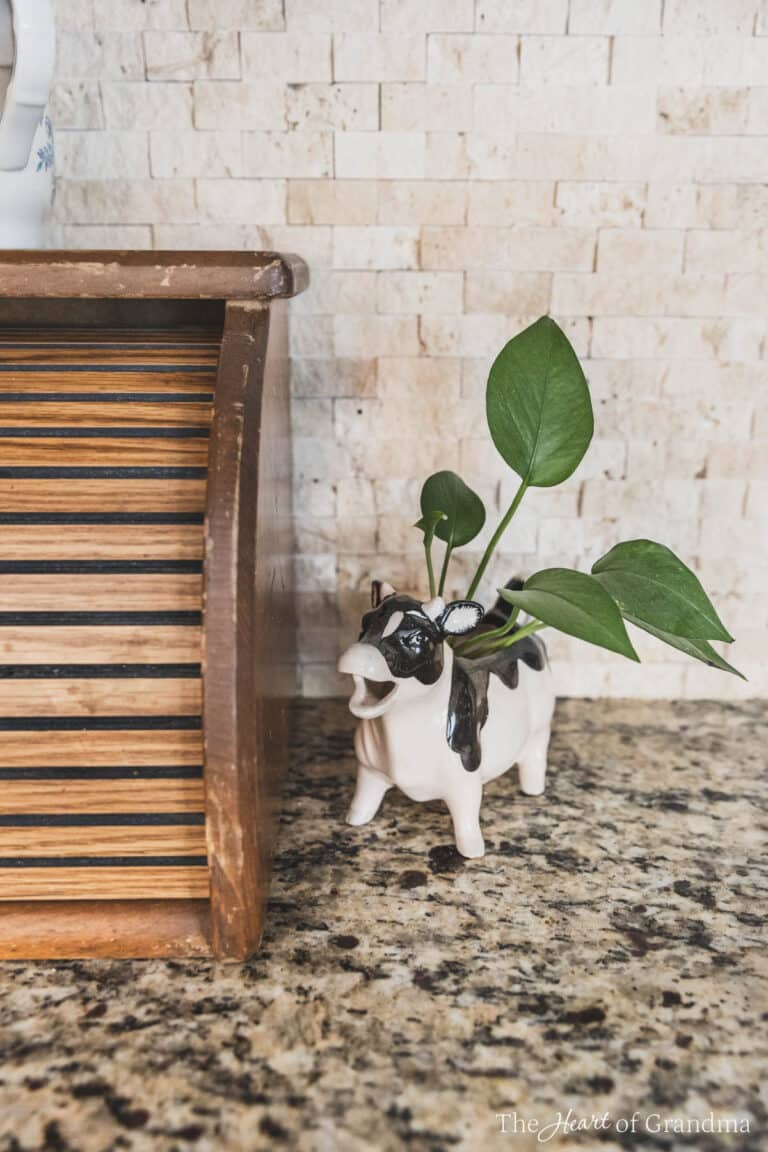 An antique cow with a plant in it sitting next to an antique bread box.